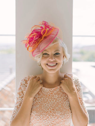 Vibrant orange and fuchsia fascinator with feathers on satin headband, perfect for weddings, races, and special occasions.