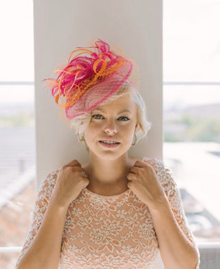 Vibrant orange and fuchsia fascinator with feathers on satin headband, perfect for weddings, races, and special occasions.