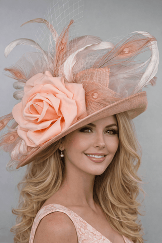 The Bloom designer derby hat by The Hat Hive featuring peach and light pink sinamay with a large floral bloom, feathers, and signature jeweled bee.