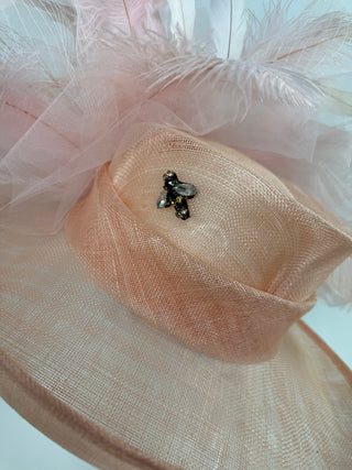 Detailed view of the handcrafted peach floral bloom and The Hat Hive's signature gold jeweled bee on the Bloom fascinator.